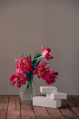 Glass vase with bouquet of beautiful tulips and white boxes on a wooden table.