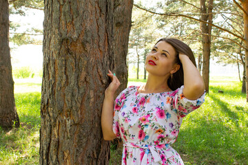 Beautiful sexy girl with short hair in dress stands near a tree in the pine forest