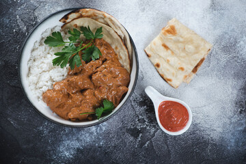 Indian chicken makhani with rice and flatbread over dark grey stone background, horizontal shot, top view