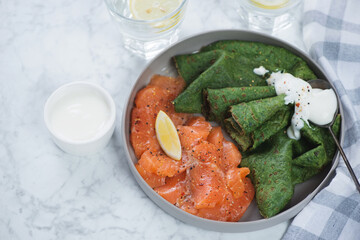 Round grey plate with salmon carpaccio and green spinach crapes, studio shot on a grey marble background, selective focus
