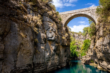 Fototapeta na wymiar Ancient arch bridge Oluk over the Koprucay river gorge in Koprulu national Park in Turkey. Panoramic scenic view of the canyon and blue stormy mountain river