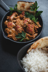 Indian butter chicken or murgh makhani in a cast-iron pan, studio shot on a black stone surface, close-up