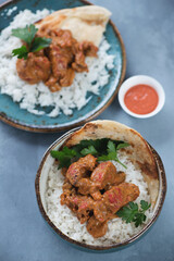Indian butter chicken masala with white rice and flatbread, elevated view over grey concrete surface, vertical shot