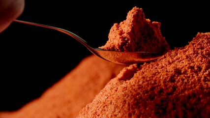 Red pepper powder is taken from a pile by a spoon