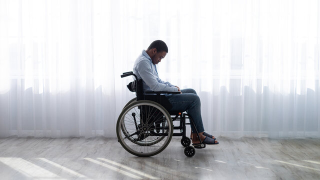 Full length of handicapped black man in wheelchair feeling desperate and lonely, suffering from depression indoors