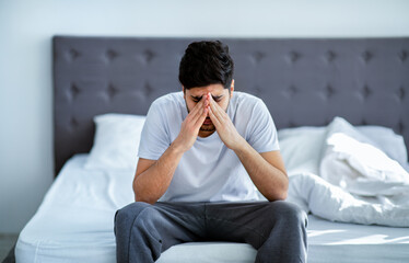 Male depression. Unhappy arab man sitting on bed and thinking about problems, closing face with hands