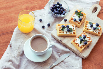 Waffles with cream and blueberries, a cup of coffee and orange juice on the table on a cloth napkin. Top view