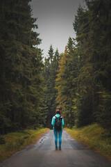Fototapeta na wymiar girl in sportswear and a tourist with a backpack stands motionless on a forest path between two different forests in the Jizera Mountains. Woman on a hike. A walk through the Czech wilderness