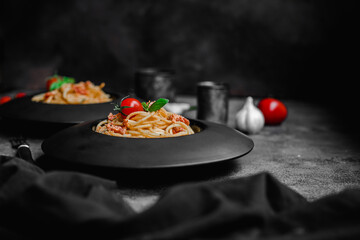 Pasta with feta cheese and baked tomatoes in a black plate. Spaghetti
