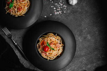 Pasta with feta cheese and baked tomatoes in a black plate. Spaghetti
