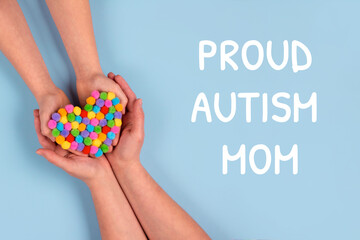 Proud Autism Mom and World Autism Awareness Day concept - autistic child's hands supported by mother holding multicolored heart on blue background. Autism spectrum disorder. Selective focus