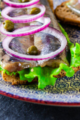 Appetizing smorrebrod with Norwegian herring, lettuce, blue onion, lemon and tomato lies on a...