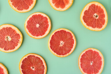 Grapefruit citrus pattern composition. Grapefruit slices with juice are scattered around on a green background with shadows. Summer or spring concept. Mock up. Top view.