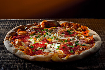 Round pizza on a wooden board. Pizza on a black table close up. Contrasting dramatic light as an artistic effect.