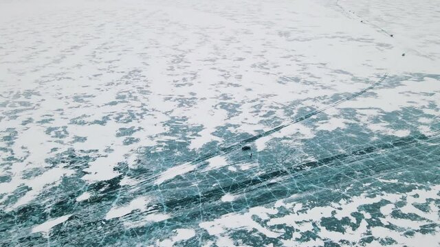The car moves in winter on a frozen lake. The blue transparent ice on the lake is partially covered with snow. Nice aerial view of a car on ice.