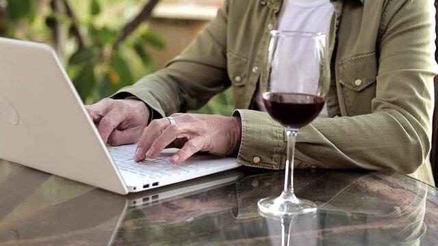 Close up of man wotking using laptop and dring wine outside. Middle selection of working proces. Alcohon during work. Freelancer
