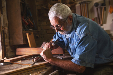 Experienced senior carpenter working in his vintage workshop.Carving and working with chisel.	
