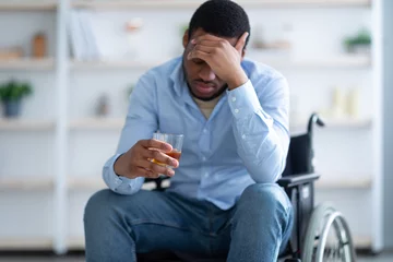 Foto op Plexiglas Disability depression and alcohol abuse concept. Young handicapped man with drink sitting in wheelchair at home © Prostock-studio