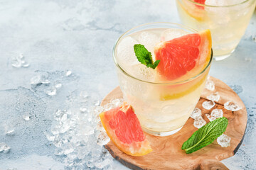 Lemonade drink made from grapefruit, soda water and mint leaves with ice on light blue slate, stone or concrete background. Healthy homemade lemonade or cocktail. Mock up. Top view.