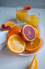 Sweet and juicy blood oranges and oranges, whole and cut on a white plate and gkasses of fresh orange juice. Fresh orange juice with Sliced oranges.