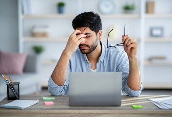 Overworked concept. Tired arab freelancer feeling exhausted while working on laptop and taking off...