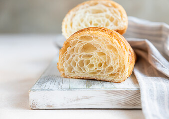 Cut in half croissant with inside texture and thin crisp layers on wooden board, light concrete background. Delicious french pastry.
