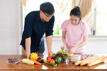 Asian young couples are cutting vegetables and smiling while cooking in kitchen at home