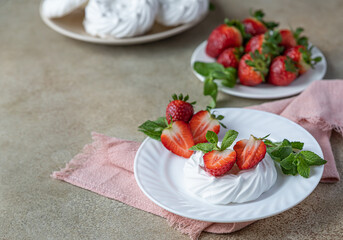 Mini meringue nest with fresh strawberries and mint on a plate, empty meringue nest and strawberries on concrete background.