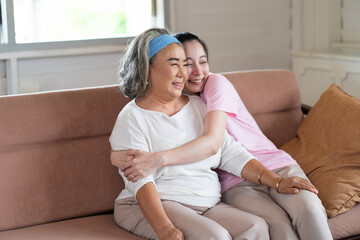 Cute Asian adult daughter embracing her mother with love in living room at home