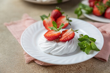 Mini meringue nest with fresh strawberries and mint on a plate, empty meringue nest and strawberries on concrete background.