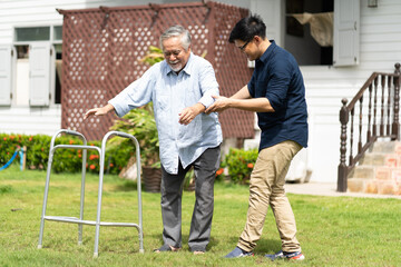 Elderly Asian father and Adult son walking in backyard. Positive Asian man caregiver helping patient