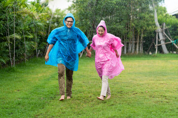 Obraz premium Happy Asian couple wearing a raincoat play in the rain outdoors at park.