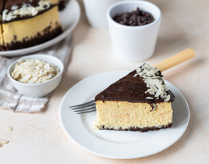 Slice of no baked creamy cheesecake with chocolate glaze and almond, light concrete background.