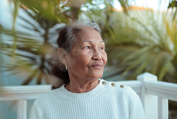 Beautiful senior filipino woman sitting in her garden, surrounded by palm trees - 422766172