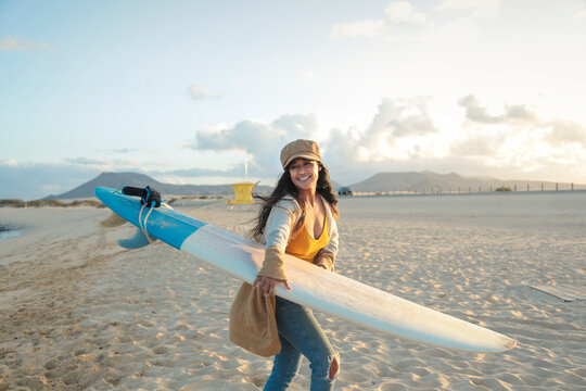 Beautiful young woman running at the beach, holding a surfboard