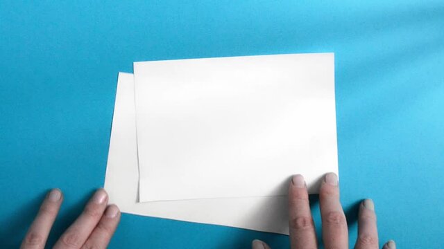 A woman's hand lays out two blank white sheets on a blue background.