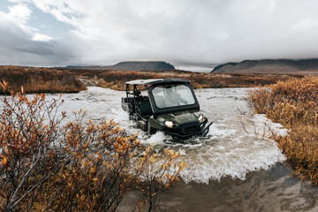 offroad quad bike atv crossing a river in Alaska hunting autumn time in alaska beautiful side-by-side during fall mountains in the background and cloudy weather © Joel