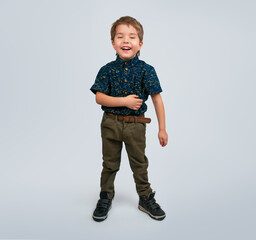 A little boy in a shirt and pants stands and laughs. Holds his stomach with laughter
