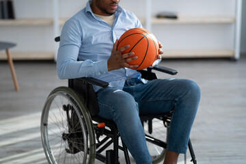 Cropped view of handicapped black man with basketball sitting in wheelchair, feeling upset over his injury at home