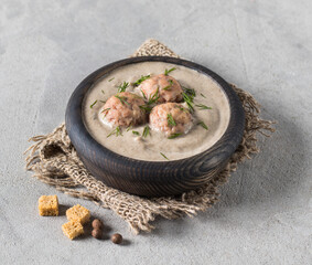 Vegan mushroom cream soup with meatballs, dill and croutons in a wooden bowl on a linen napkin on a light gray background