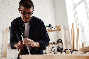 Middle-aged man carpenter working in a workshop with chisel and hammer