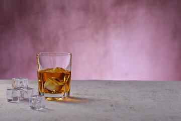 Whiskey im Glas mit Eiswürfel vor einer Betonwand