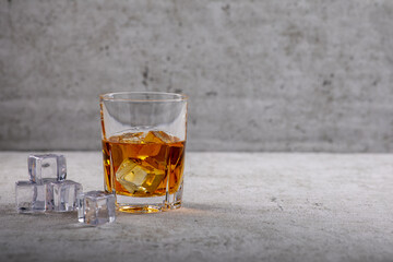 Whiskey im Glas mit Eiswürfel vor einer Betonwand