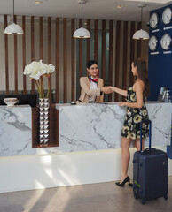 Young travelers talking and check-in register information with woman receptionist worker standing in counter hotel reception counter desk at lobby modern hotel..
