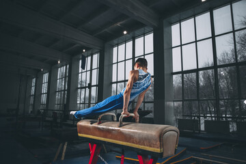 Fototapeta na wymiar Little male gymnast training in gym, flexible and active. Caucasian fit little boy, athlete in sportswear practicing in exercises for strength, balance.