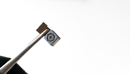 Close-up on the mobile phone camera module. Close-up tweezers or a clip holds the smartphone lens in a studio shot against a white background with copy space