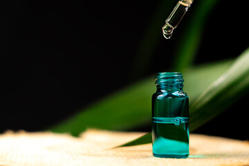 Cosmetic pipette over a bottle of serum on a wooden table against a background of green plants on a black background with copy space. Concept of cosmetology, medicine