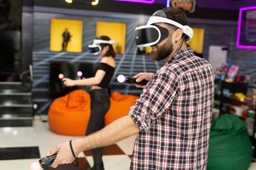 Friends, a man and a woman use a virtual reality headset with glasses and hand motion controllers in the play area. Modern technologies concept image. © Studio Peace