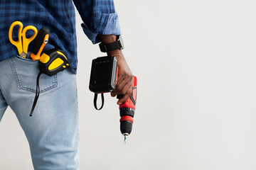 Black repairman holding electric drill in hand, in pocket measuring tape, screwdriver and scissors,...