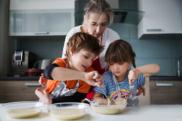Two kids and mom cook dough together, bake pie in domestic kitchen. playful siblings helping to...